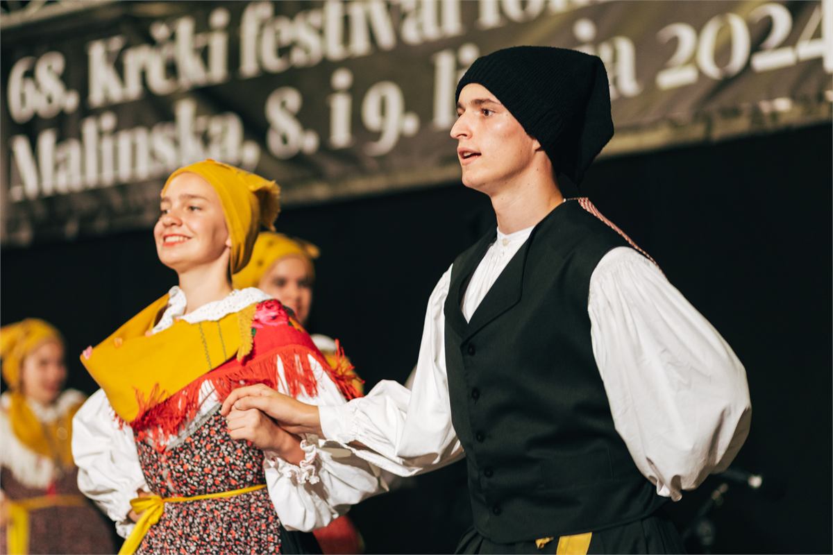 Mlađahni plesni par u nošnjama drži se za ruke pred pozornicom Krčkog festivala folklora