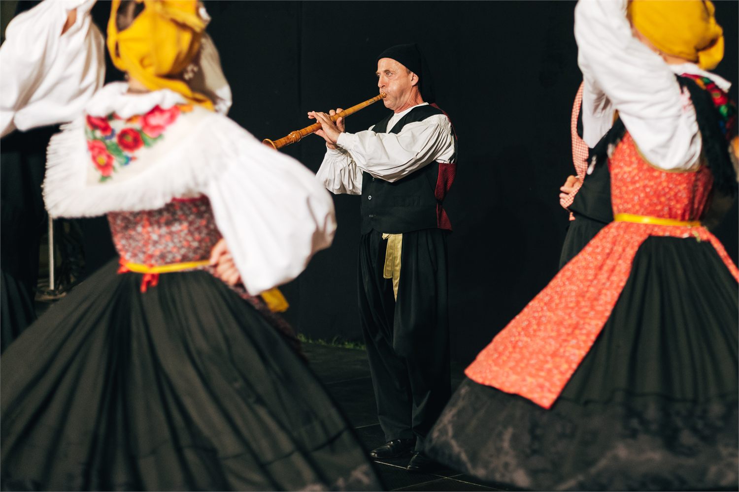 Sopac svira sopilu na pozornici dok se s obje strane vrte plesačice u krčkim nošnjama
